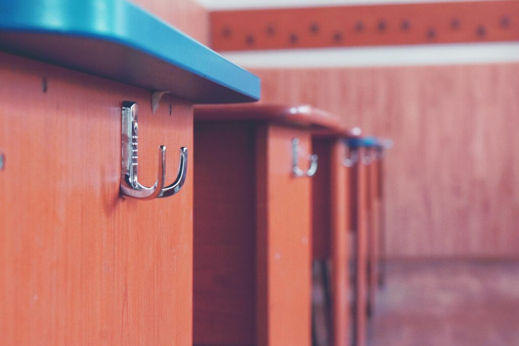 A detailed view of a metal hook on a wooden desk in a classroom setting.