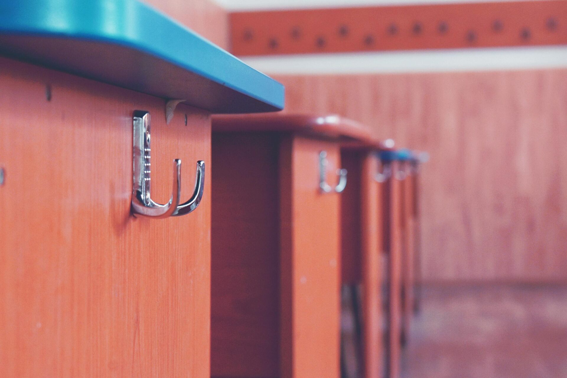 A detailed view of a metal hook on a wooden desk in a classroom setting.